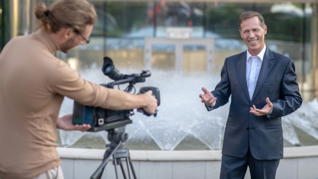 Filmy wizerunkowe to skuteczne narzędzie marketingowe. Na zdjęciu biznesmen nagrywa film wizerunkowy z operatorem kamery.